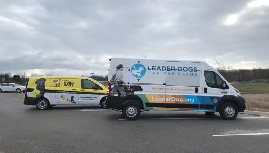 Une camionnette aux couleurs des chiens-guides d'INCA (à gauche) garée à côté d'une camionnette de Leader Dogs for the Blind des États-Unis (à droite).