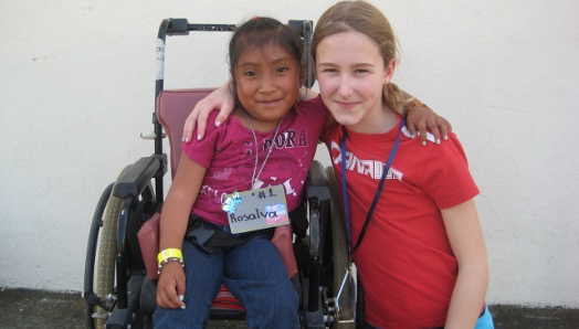Au Guatemala, une jeune Veronika s'accroupit à côté d'une jeune fille en fauteuil roulant. Elles se tiennent par le bras et posent pour la photo.