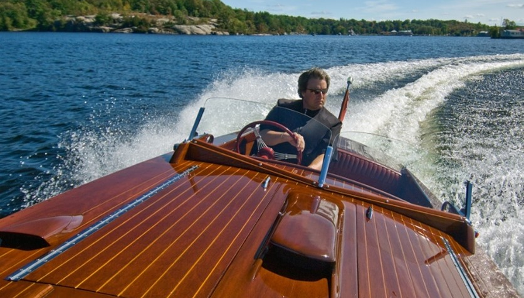 Un homme au volant d’un bateau en bois sur un lac de Muskoka.