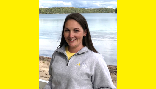 Lindsay Garrett, gestionnaire de programme, se tient sur la plage de Lake Joe et porte un sweat-shirt gris à fermeture éclair trois-quarts.