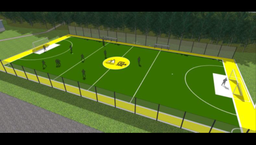 Un aperçu du nouveau terrain de soccer en gazon synthétique, un terrain de 40 m x 20 m. Un filet noir de 2 m de haut sur les côtés, avec le logo de Lake Joe d'INCA (un voilier blanc) dans un cercle jaune au centre du terrain, des filets de but de soccer à chaque extrémité et une bordure jaune autour du terrain.