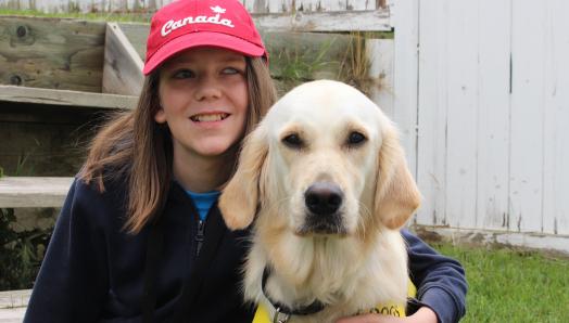 Zach et Elsie, son chien compagnon d'INCA, assis dans leur cour. Elsie porte son gilet jaune de chien compagnon d’INCA et Zach l’entoure de son bras