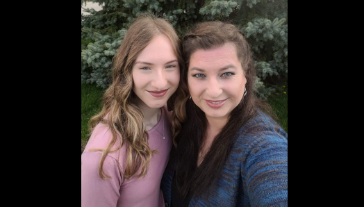 Emma (left) and Michelle (right) smile and pose for a photo in front of a beautiful green tree.