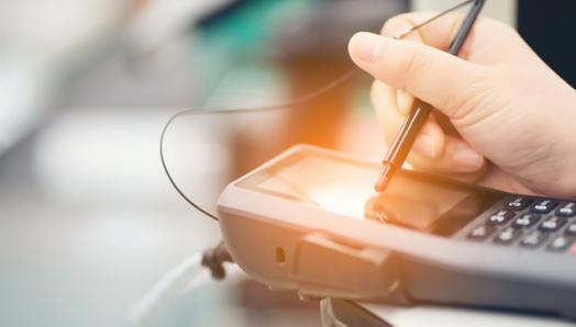 A close up of a person’s hand using a stylus pen to make a selection on the touch screen surface of a payment terminal.