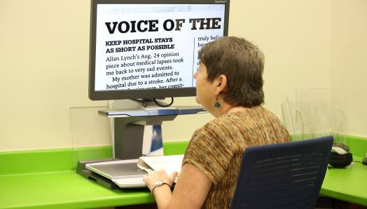 A woman sits at a CCTV and reads an enlarged document displayed on the screen.