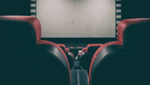 An empty movie theatre. Rows of chairs are stacked in front of dark movie screen.