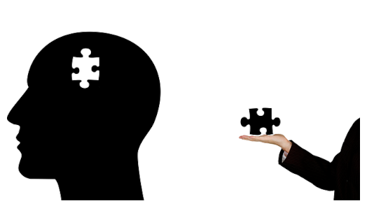 Illustration/silhouette d’une tête chauve. Il manque une pièce de puzzle à l’intérieur de la tête. À droite de la tête, une main étrangère sort du cadre et tient la pièce manquante du puzzle.