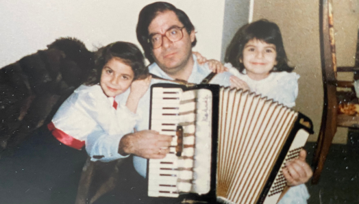 Une photo de la fin des années 80. Dimitrios joue de l'accordéon. Une jeune Angela est assise à gauche. Sa sœur est assise à droite.
