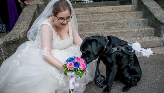 Une photo de Christine le jour de son mariage, agenouillée à côté d'Edie dans sa robe de mariée, tenant un magnifique bouquet de fleurs roses et bleues.