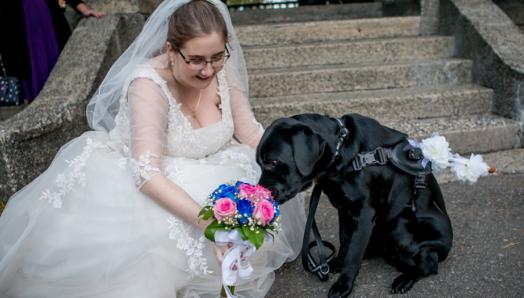 Une photo de Christine le jour de son mariage, agenouillée à côté d'Edie dans sa robe de mariée, tenant un magnifique bouquet de fleurs roses et bleues. 