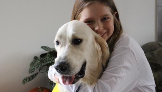 Dani assise et serrant dans ses bras son chien George, un Golden Retriever portant le gilet jaune vif des chiens compagnon d'INCA, tous deux souriant pour la prise de phot