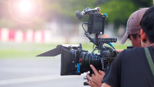 A cinematographer holds a large camera and films. 