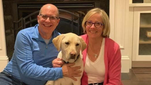 Un labrador blond assis sur le sol entre Patti Sullivan et son mari Patrick.