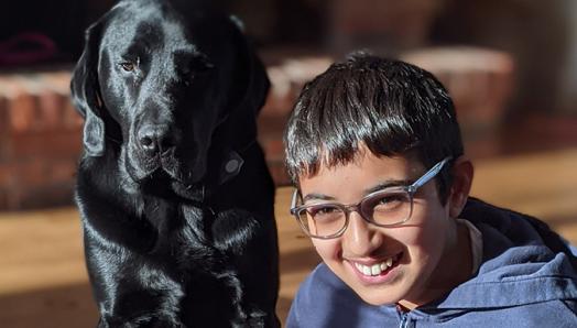 Surya sitting cross-legged on the floor smiling, with Isaiah sitting next to him in the sun.