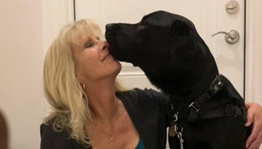 Karen, assise sur le palier intérieur d’entrée, reçoit de Healey un baiser sur le visage, son chien-guide INCA.