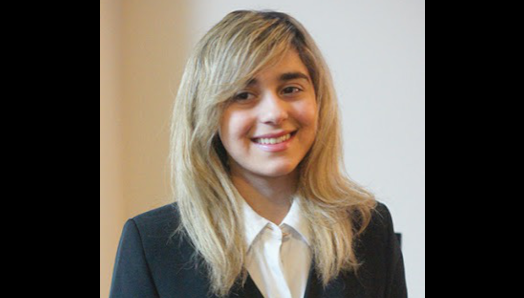 Avesta poses for a professional headshot. She is wearing a black blazer and a white dress shirt. 