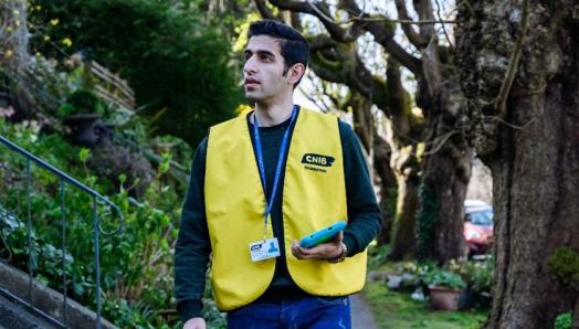 Collecteur de fonds d'INCA portant un gilet jaune, un badge d'identification et une tablette.