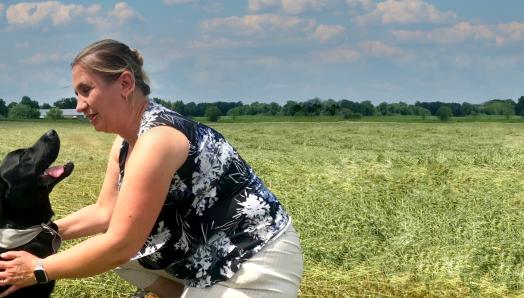 Louise kneeling on a sunny field, with her arms around Jess, who is sitting and smiling up at Louise. 