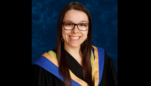 Une photo de Danica Frappier lors de la remise des diplômes. Elle est souriante et porte une robe de graduation avec une étole aux accents bleus, jaunes et dorés.