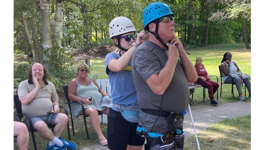 Un membre du personnel aide à fixer le casque d'un invité au pied de la tour d'escalade du camp.