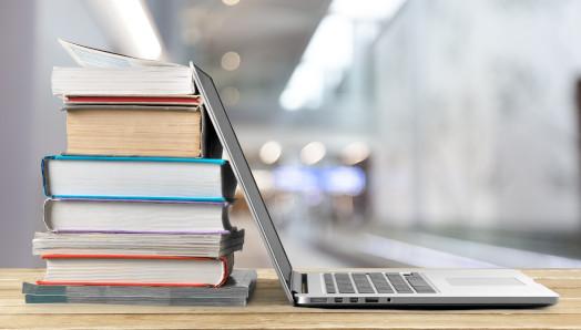 A stack of books beside a laptop on a wooden table.