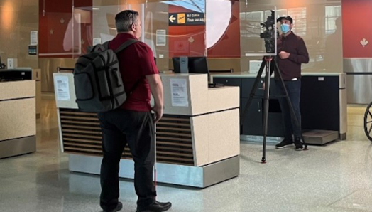 Duane Morgan, vice-président d’INCA pour le Canada atlantique, est debout devant une borne d’aéroport, pendant qu’un caméraman filme en arrière-plan.