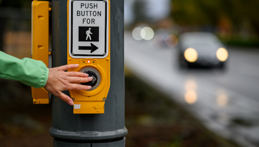 Une main appuie sur un bouton de passerelle pour piétons en attente de traverser une intersection.