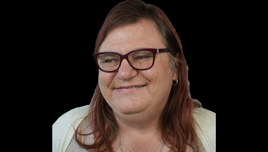 A headshot of Tina against a black background. Tina is smiling and wears glasses.