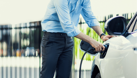 Dans une station de recharge publique, un homme tient une prise de recharge pour véhicule électrique et recharge sa voiture.