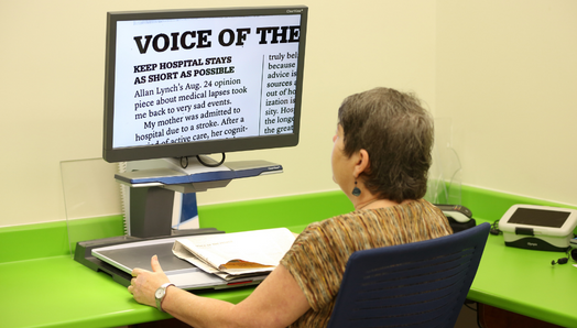 Une femme est assise devant un téléviseur en circuit fermé et lit un document agrandi affiché à l’écran.