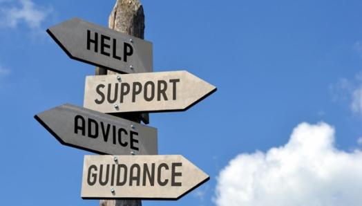 Panneau de signalisation avec les mots « aide », « soutien », « conseils », « orientation » en anglais sur des flèches en bois pointant dans différentes directions avec un ciel bleu en arrière-plan.