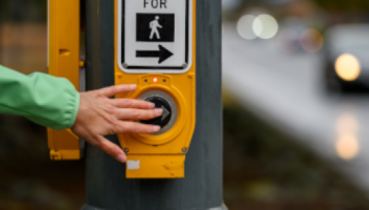 Une main appuie sur le bouton d’un passage piétonnier pour traverser une intersection.