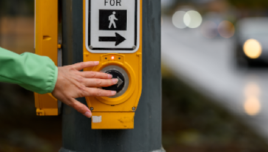 A hand pushes a pedestrian crosswalk button to cross an intersection.