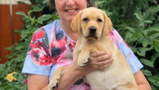 Eileen holds an 8-week-old Bridget. They stand outside against a lush green garden. 