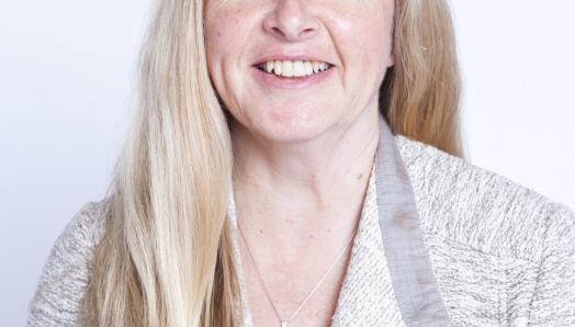 A professional headshot of Diane Bergeron. She is smiling, sitting in In front of a white background, and wears a grey and white cardigan. 