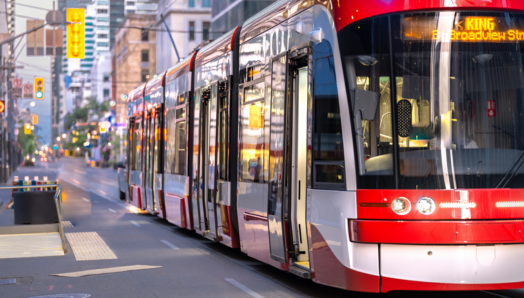 A streetcar glides along a busy city street and approaches a stop.