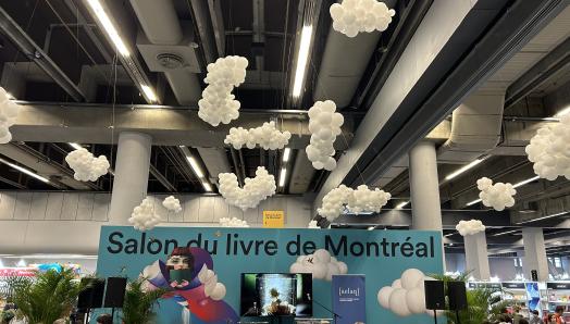 Scène du Salon du livre de Montréal avec des ballons blancs accrochés au plafond qui forment des nuages.