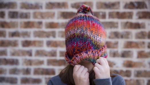 A young girl pulls her colourful winter hat over her face.