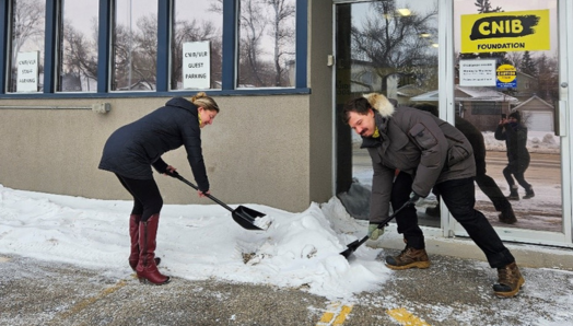 Amanda Titman et Dallas Lynch, membres du personnel d'INCA et de RDVC, utilisent les pelles de la campagne « Déneiger la voie! » pour déneiger un emplacement de stationnement accessible devant le bureau d'INCA à Saskatoon.