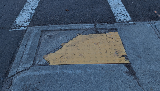 Des indicateurs tactiles de surface de marche (TWSI) situés du côté le plus proche de la route à Charlottetown, qui ont été aplatis et endommagés. Il n'y a pas de TWSI de l'autre côté de la route.