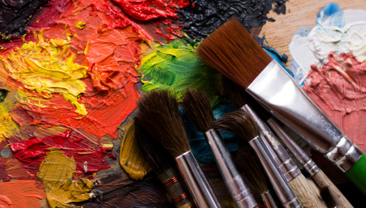 Une peinture murale colorée peinte à la main avec divers pinceaux posés dessus. La peinture abstraite est épaisse et texturée, dans des couleurs vives comme le rouge, le jaune et le vert.