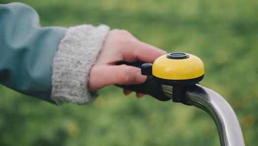La main d'une personne fait sonner une sonnette de vélo jaune. La cloche est montée sur le guidon de la bicyclette.