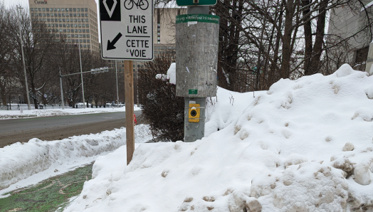 Un très gros tas de neige bloque l'accès à un trottoir et au bouton du signal piéton accessible à un passage pour piétons à Ottawa, en Ontario.
