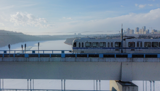 Un train léger d’Edmonton traverse un pont. Le pont s’élève au-dessus d’une étendue d'eau gelée, avec l’horizon d’Edmonton en arrière-plan.