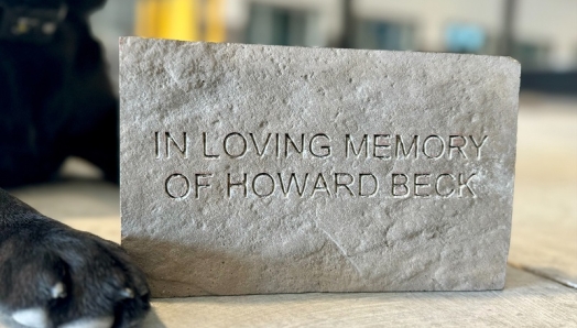 Gros plan d'une patte de chien à côté d'une brique sur laquelle on peut lire « In Loving Memory of Howard Beck ».