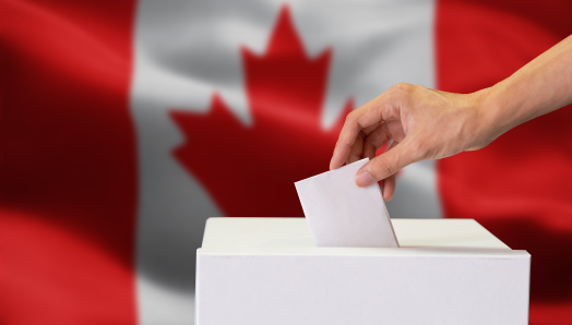 Une personne déposant son bulletin de vote dans une urne. Un drapeau canadien en arrière-plan.