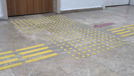 Un sol carrelé avec un pavage tactile/des indicateurs tactiles de surface d'orientation Le pavage est constitué de points et de lignes jaunes en relief. 