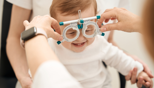 Un optométriste procède à un examen de la vue sur un jeune enfant. Il tient d'une main un cadre d'essai optométrique devant le visage de l'enfant.