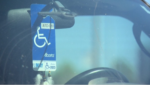 Un permis de stationnement pour personnes à mobilité réduite de l'Alberta est accroché au rétroviseur d'une voiture. La photo a été prise depuis l'extérieur du véhicule, en regardant à travers le pare-brise.